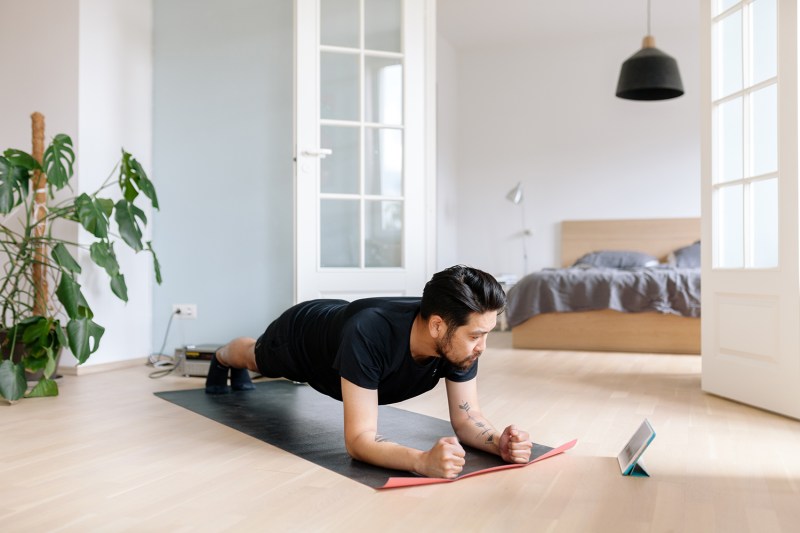 Man doing plank exercise on a mat with an iPad.
