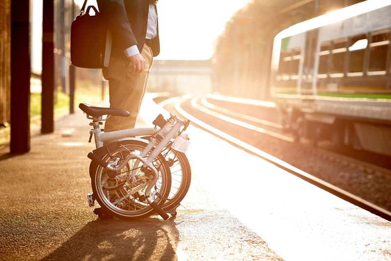 A man standing beside his folding bike at the train station.