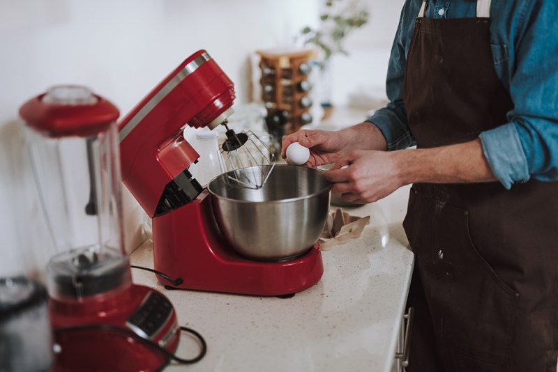 Person cracking egg on the bowl of electric stand mixer