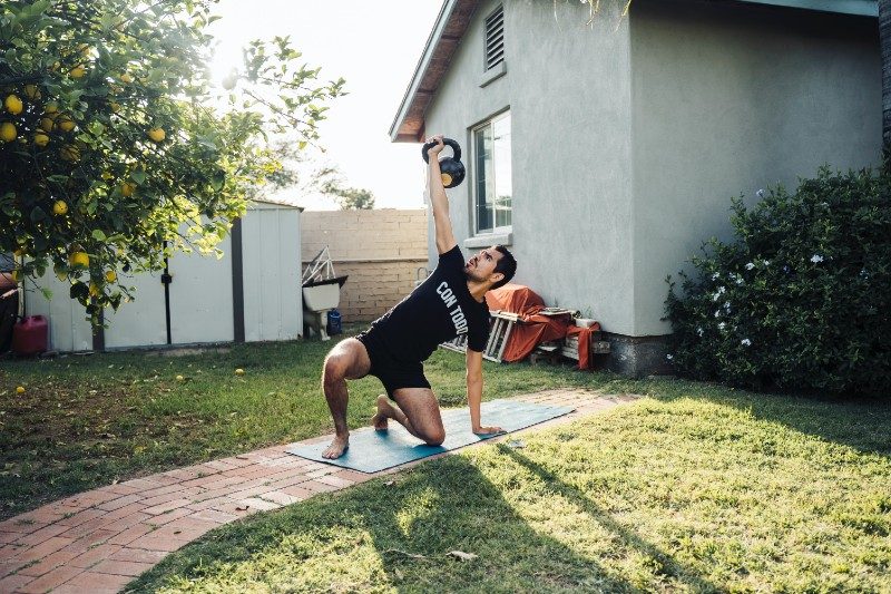 Man lifting a kettlebell on a yoga mat outside