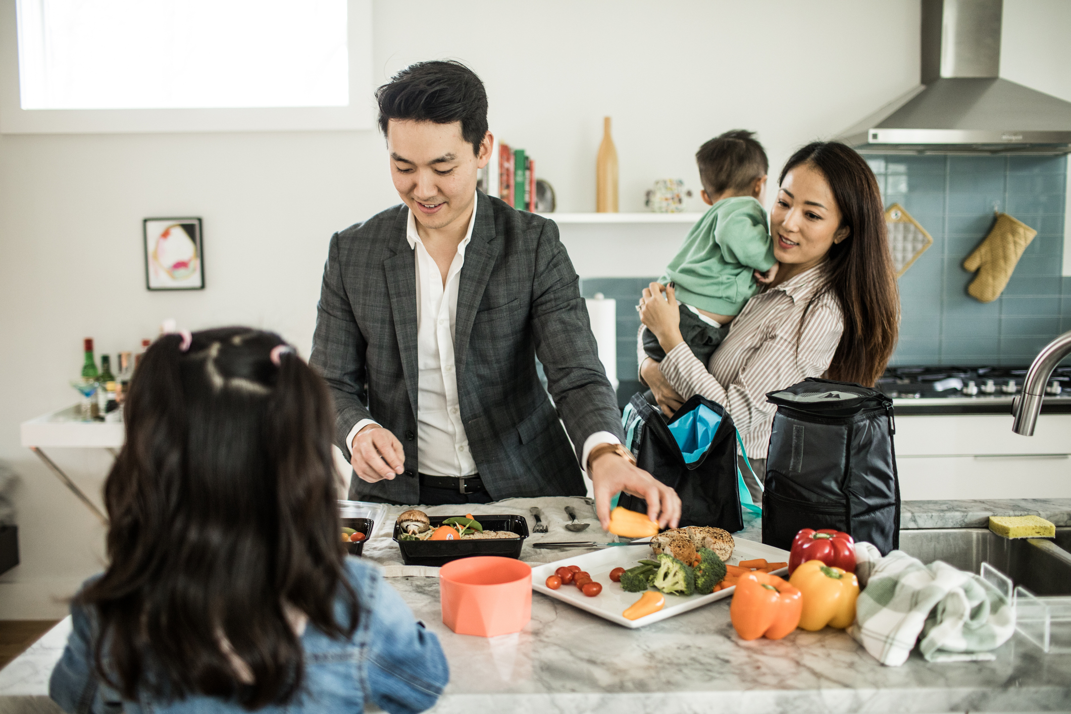 A family of four is preparing a meal in the kitchen for their father's lunchbox.