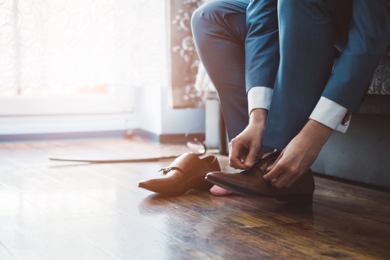 man in a suit putting on brown dress shoes.