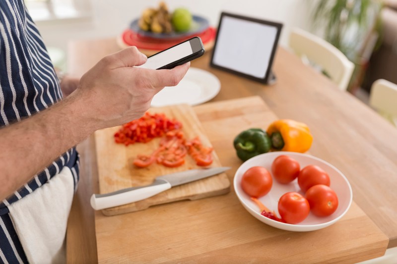 Man using smartphone while preparing food in the kitchen