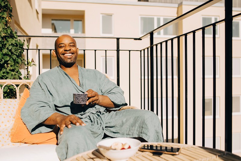Happy mature man having coffee sitting on sofa on balcony