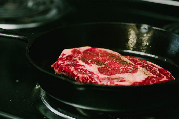 A ribeye steak cooking in cast iron pan.
