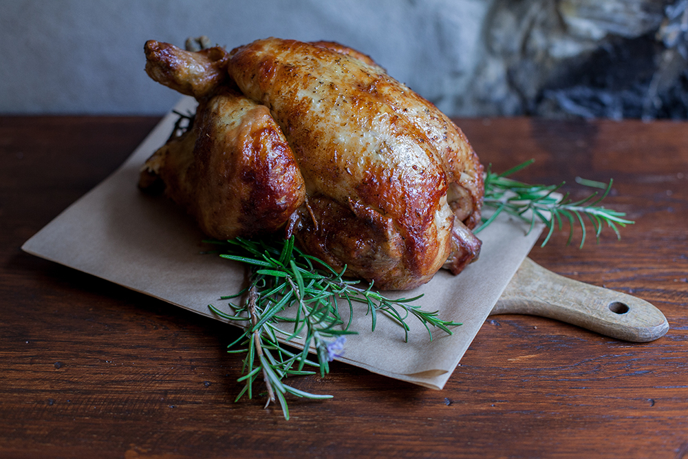 Close-up of a roasted chicken on a cutting board at a table