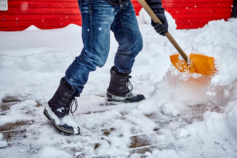 A person using a yellow snow shovel to clear up snow.