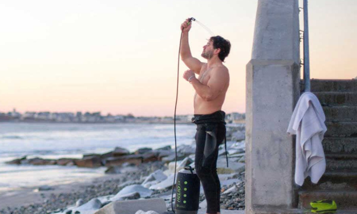 Man using a portable outdoor shower near the beach.