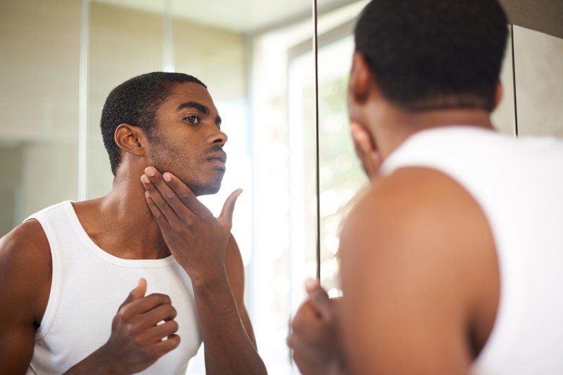 Guy looking at his skin in mirror.