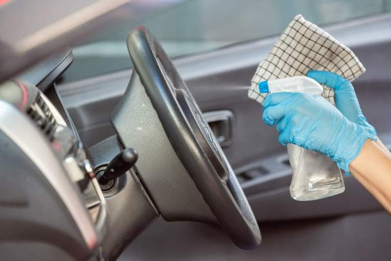 Una persona con guantes rociando un limpiador en el volante.