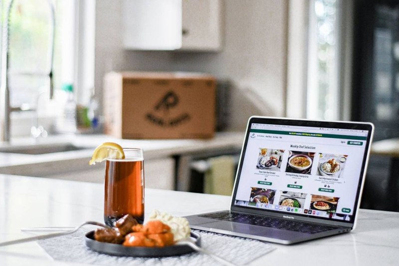 A healthy dish and a drink with towel and laptop on a kitchen counter.