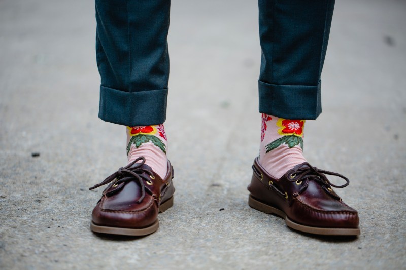 A guy standing, wearing loafers partnered with floral socks and a pair of pants.