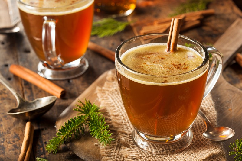 two mugs of hot buttered rum with cinnamon sticks.