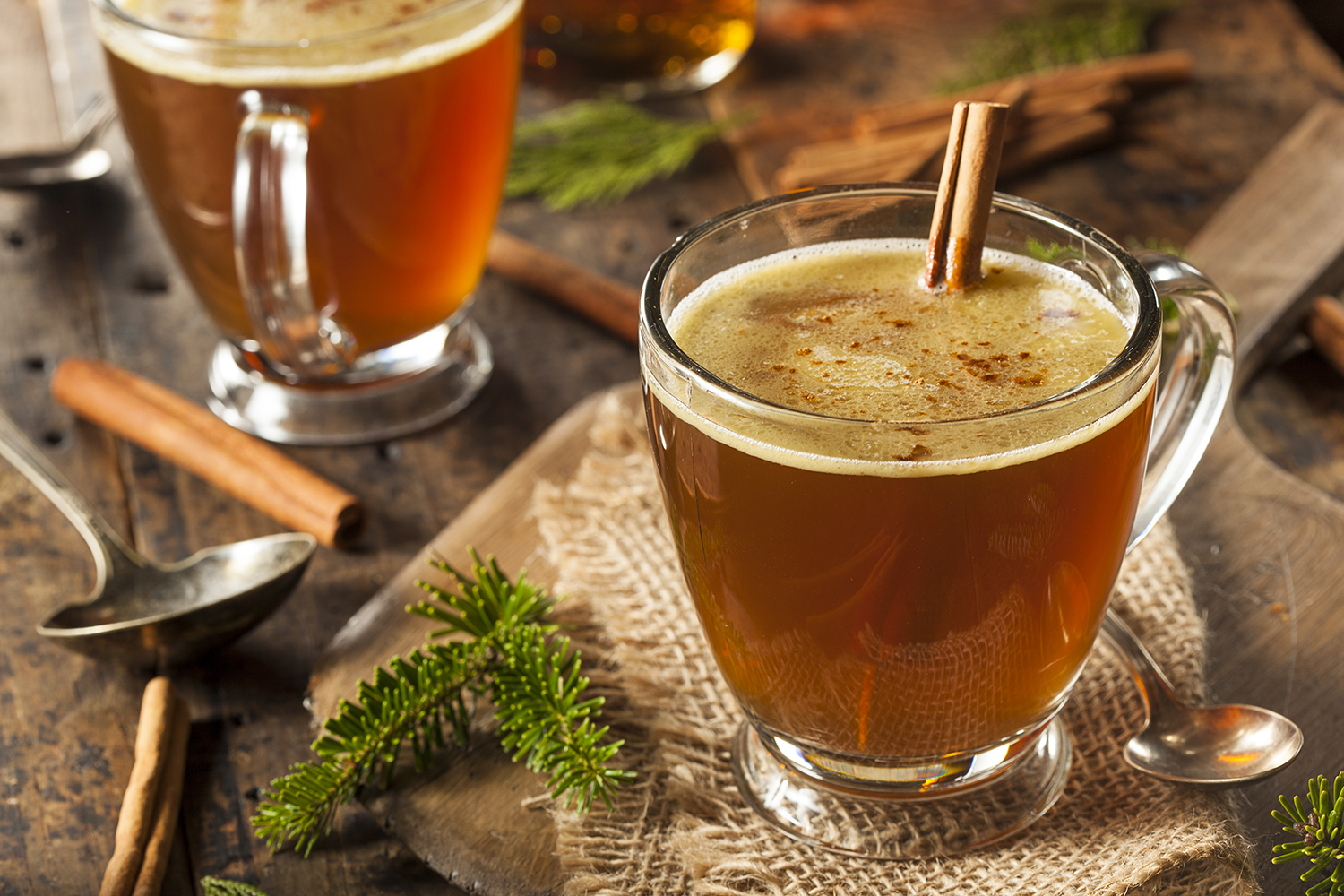 two mugs of hot buttered rum with cinnamon sticks.