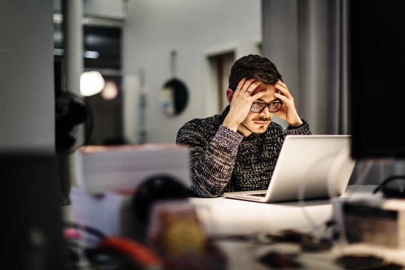 Man with his hands on his temples as he is trying to focus with a laptop in front of him.