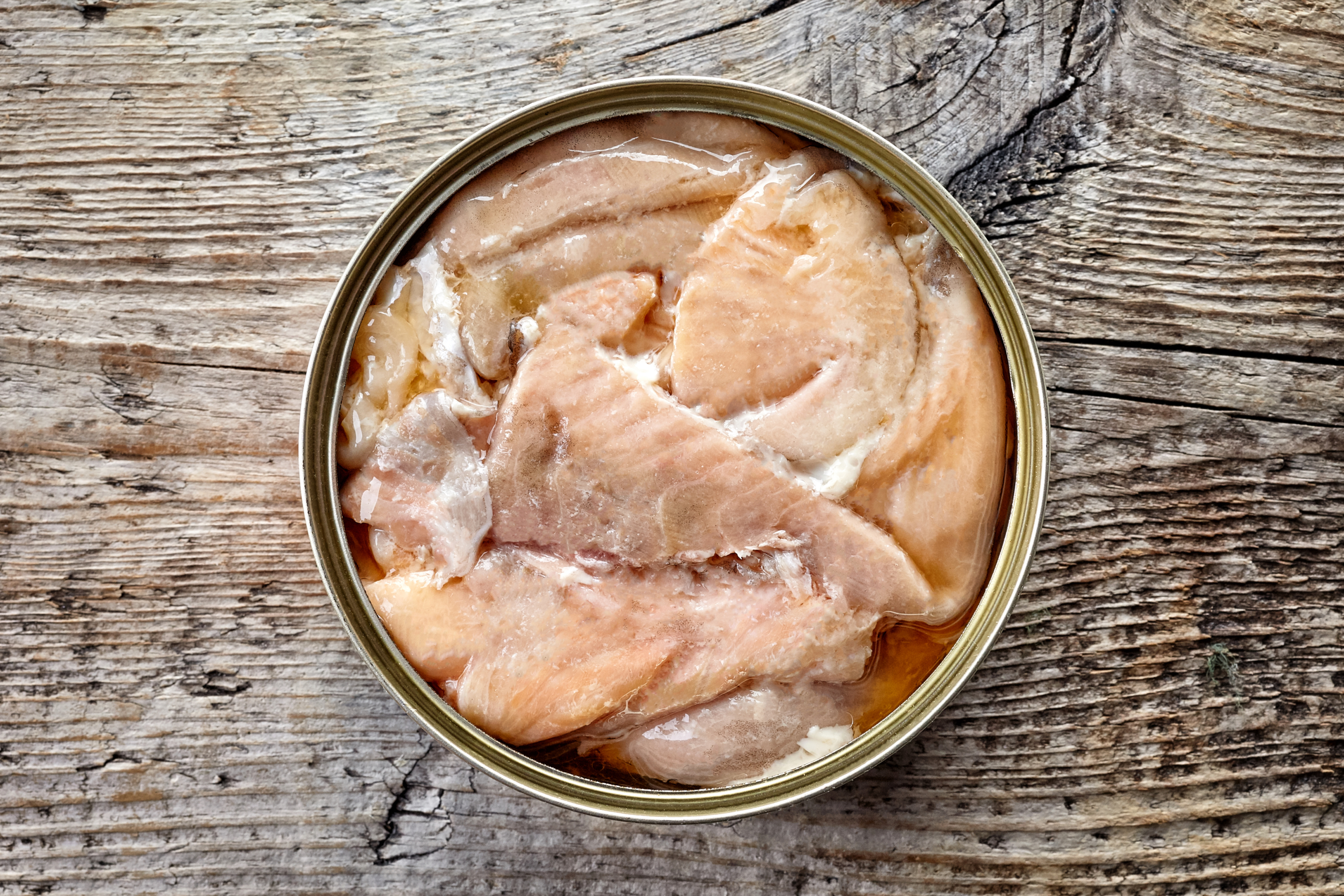 Open tin can, canned salmon, on wooden background, top view