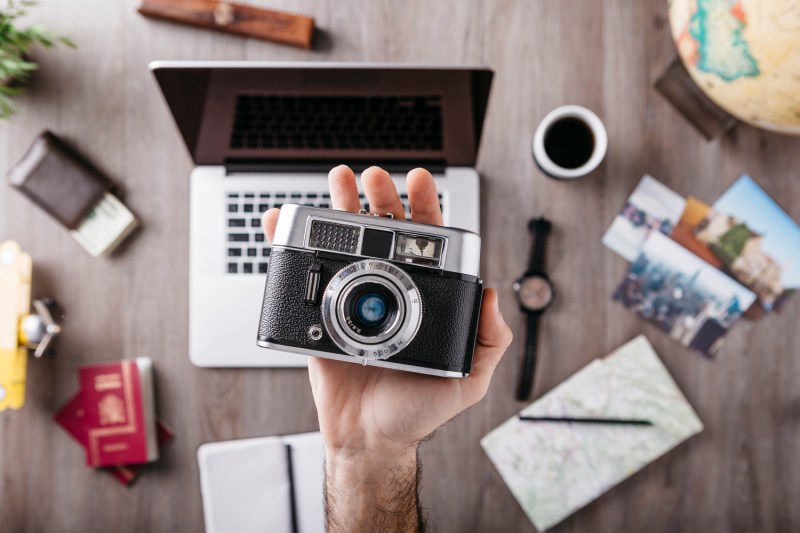 Hand holding a camera with various objects in the background.