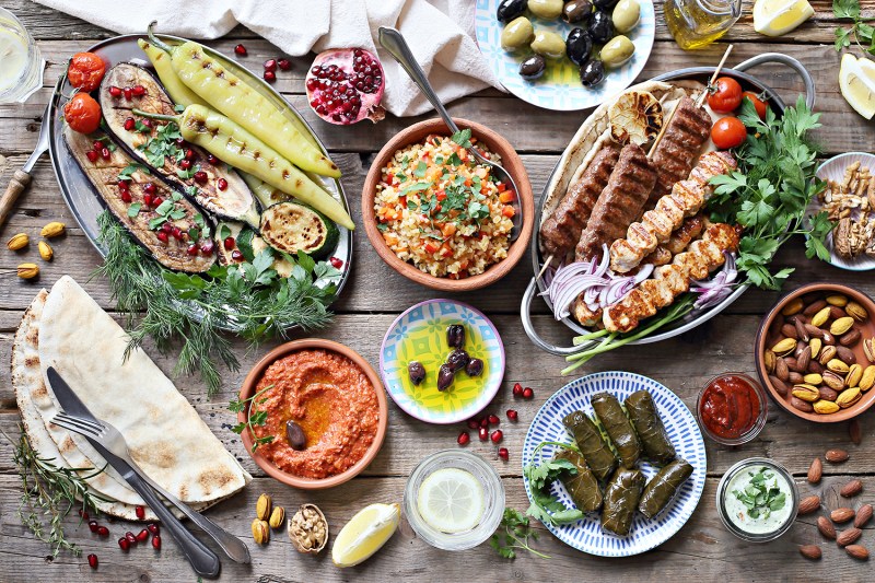 Middle Eastern, Arabic, or Mediterranean dinner table with grilled lamb kebab, chicken skewers with roasted vegetables and appetizers variety serving on rustic outdoor table