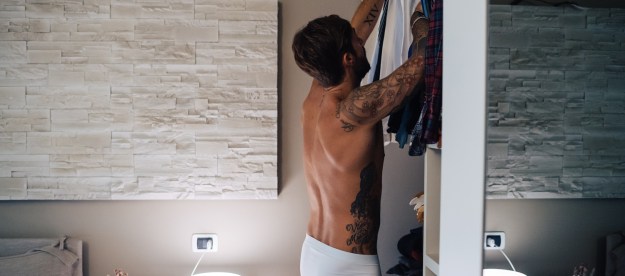 Man in underwear getting dressed in a bedroom.