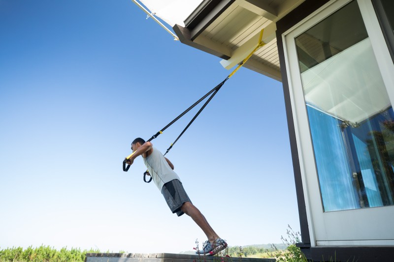 Man doing a TRX Workout outside his house during a sunny day.