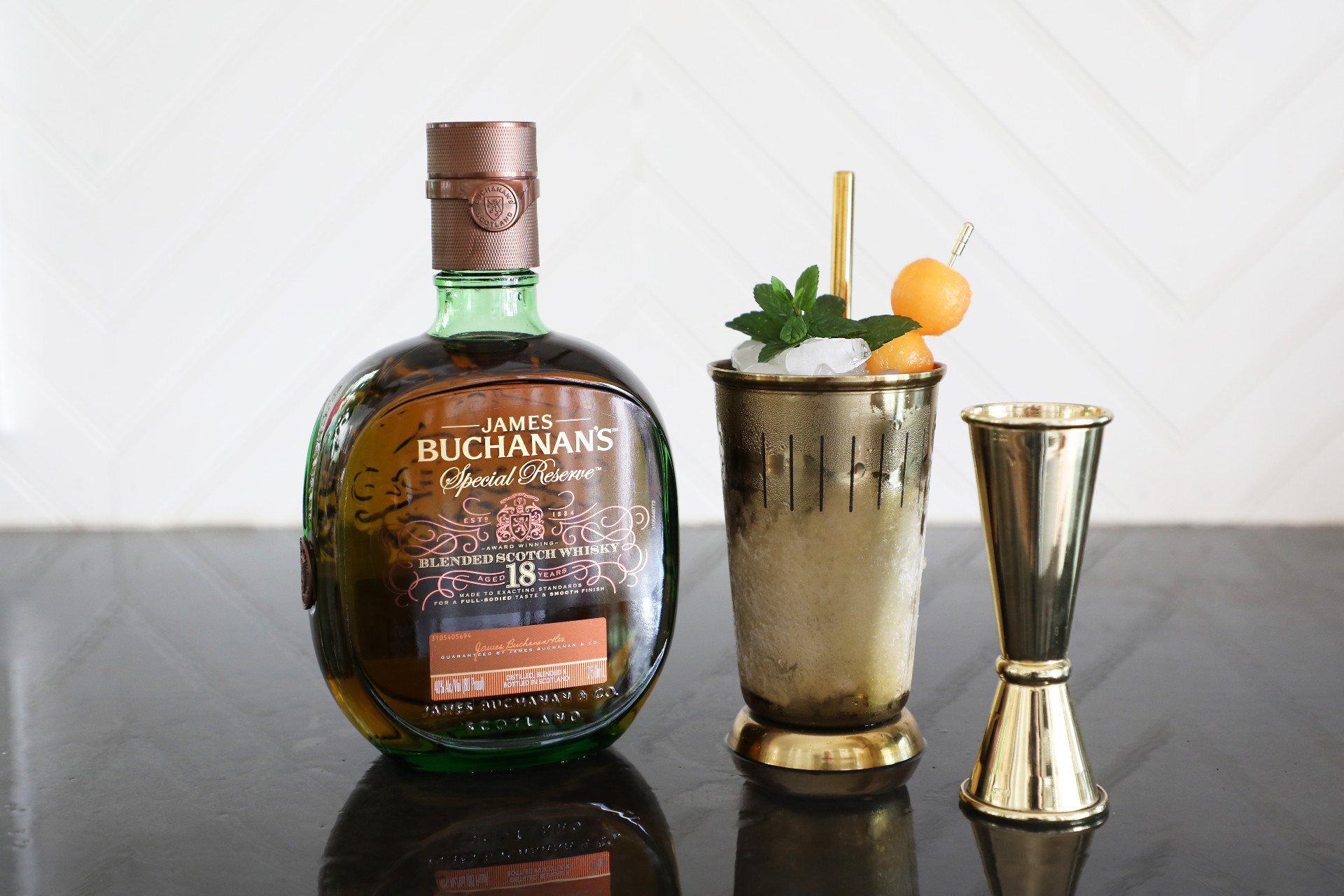 A bottle of Buchanan’s Special Reserve beside a Spring Fling Julep Cocktail with mint leaves and melon balls and a pouring sprout. 