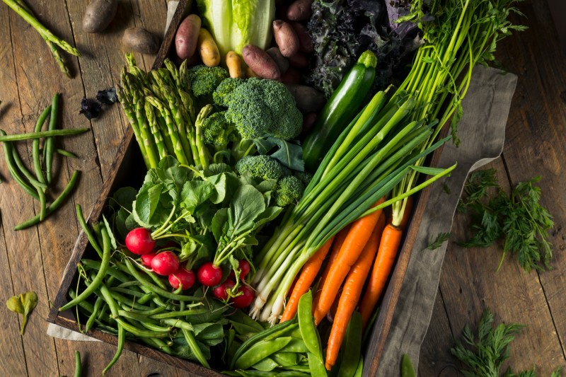 Carrots, broccoli, and spring onions among other spring vegetables laid out in a wooden table