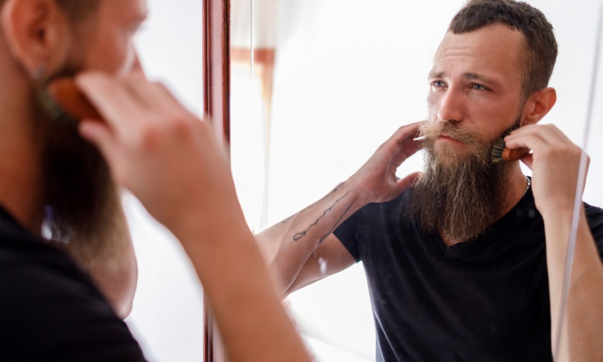 Man brushing his beard in the mirror
