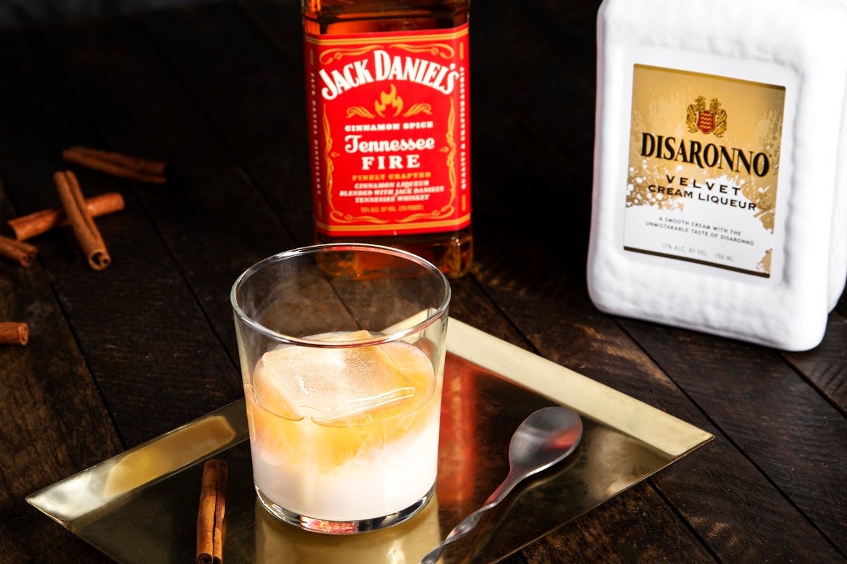 A glass of Velvet Fire Cocktail beside a spoon with Disaronno Velvet and Jack Daniel's Tennessee Fire behind it.