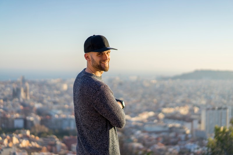 Spain, Barcelona, smiling young man standing on a hill overlooking the city