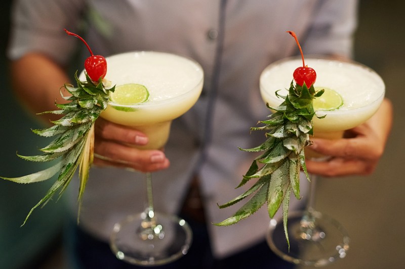 man holding two glasses of pina coladas. 