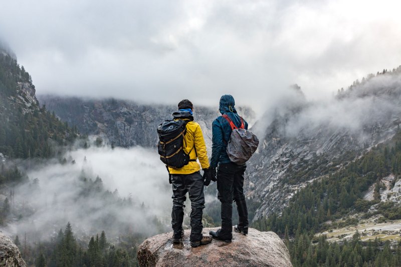 Two men outdoor gear standing on a rock, looking out into a foggy mountain valley.