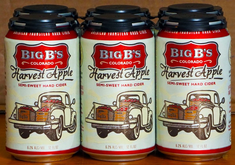 A six pack of Big B's Harvest Apple Hard Cider, lemon yellow cans with a vintage pickup loaded with apple crates.