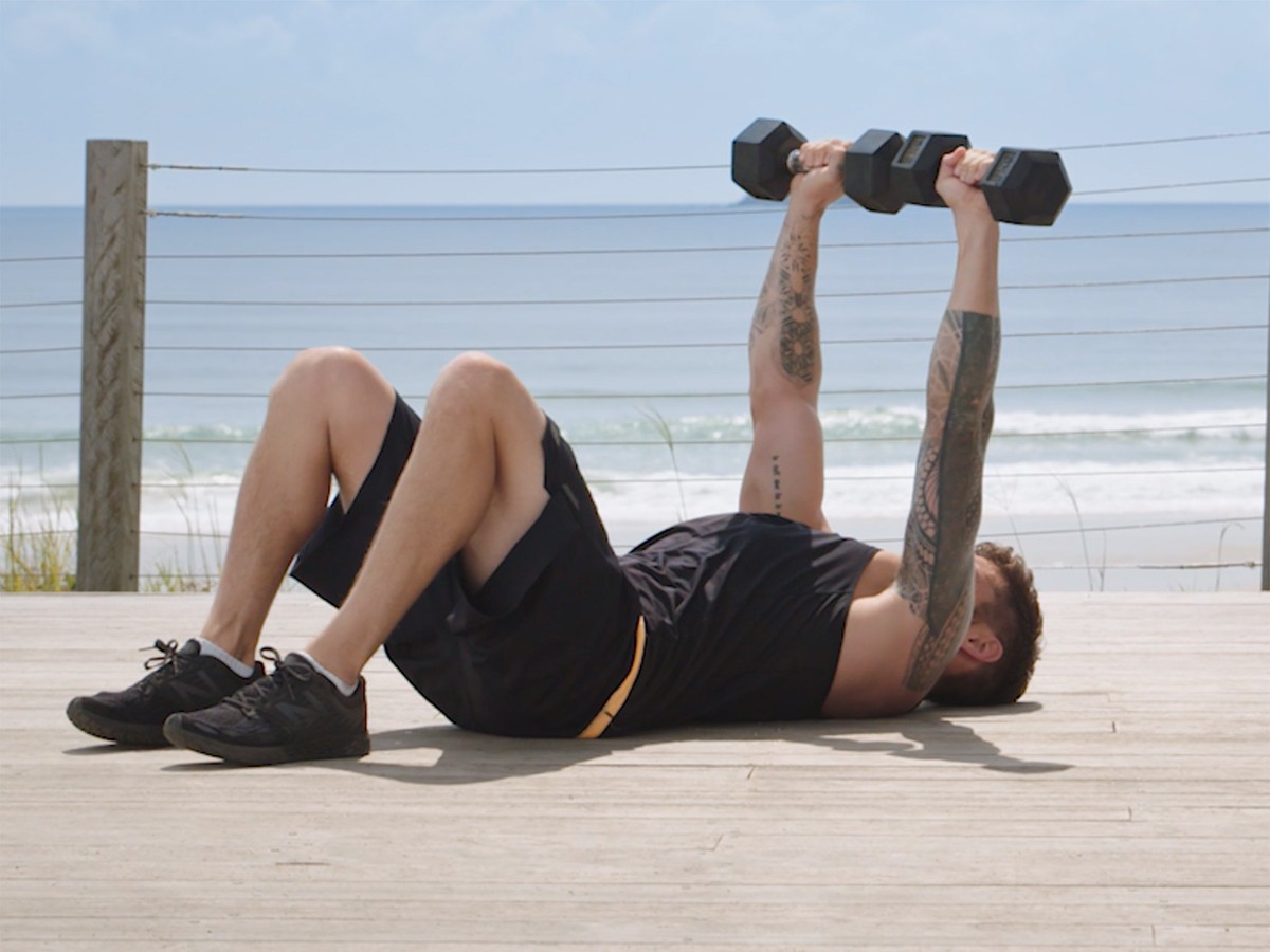 man performing dumbbell chest press near the ocean
