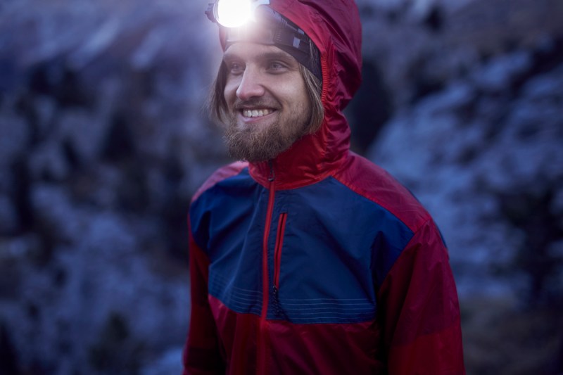 Young smiling man wearing a bright headlamp in the outdoors.