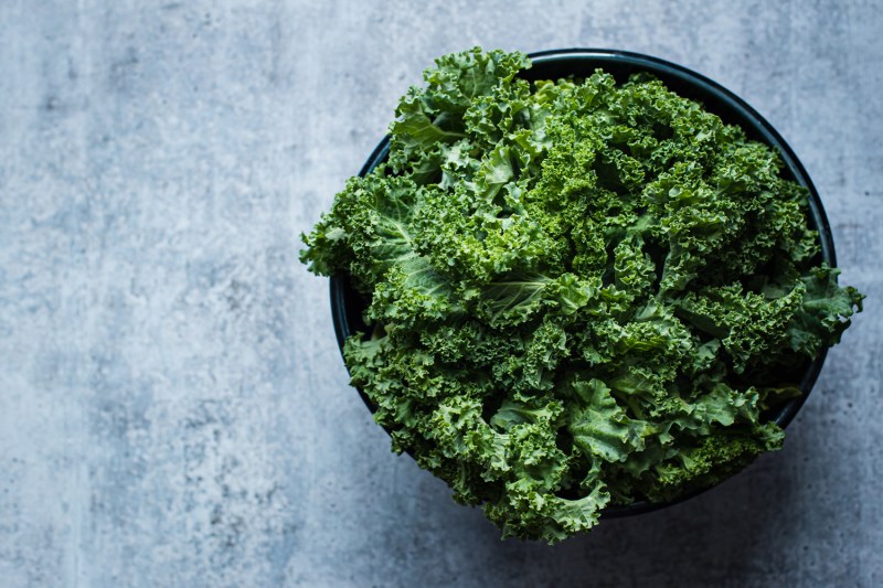 A bowl of kale on blue table.