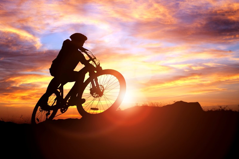 Mountain biker silhouette against the sunset concept for achievement, conquering adversity and exercising