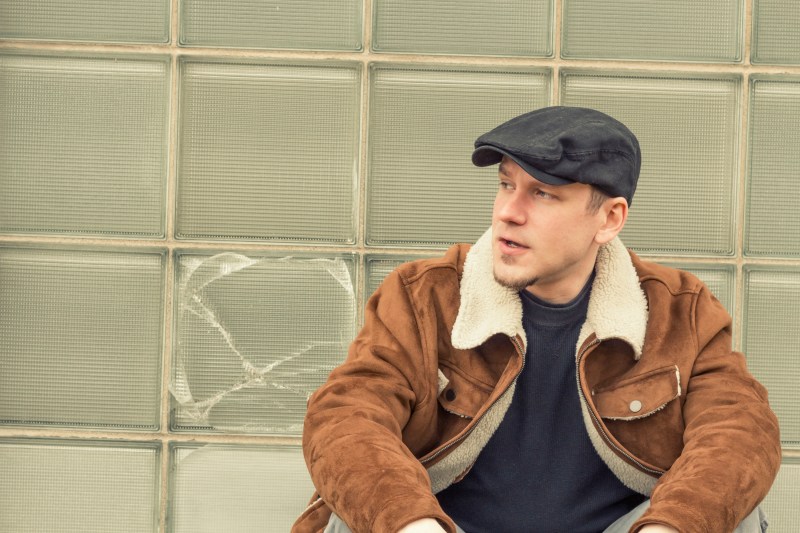 Cool guy in aviator jacket and newsie cap relaxes against a glass wall
