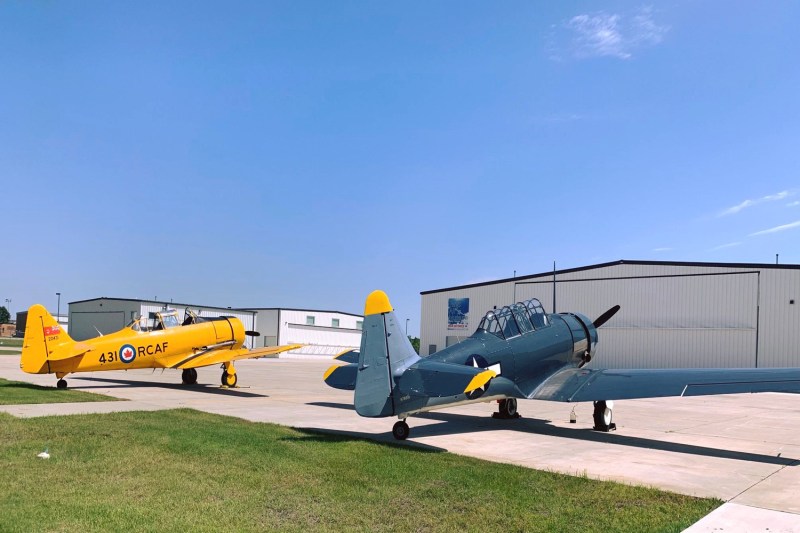 Two fighter planes, one yellow one black, sit facing an aircraft hangar.