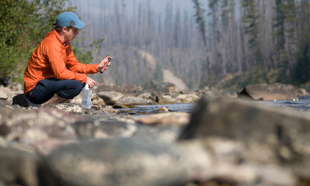 Young man using a portable water filter near a backcountry stream.