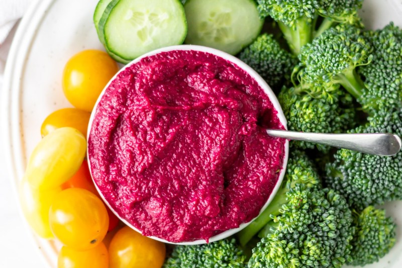 Bowl of hummus surrounded by cucumber slices, broccoli, and grapes