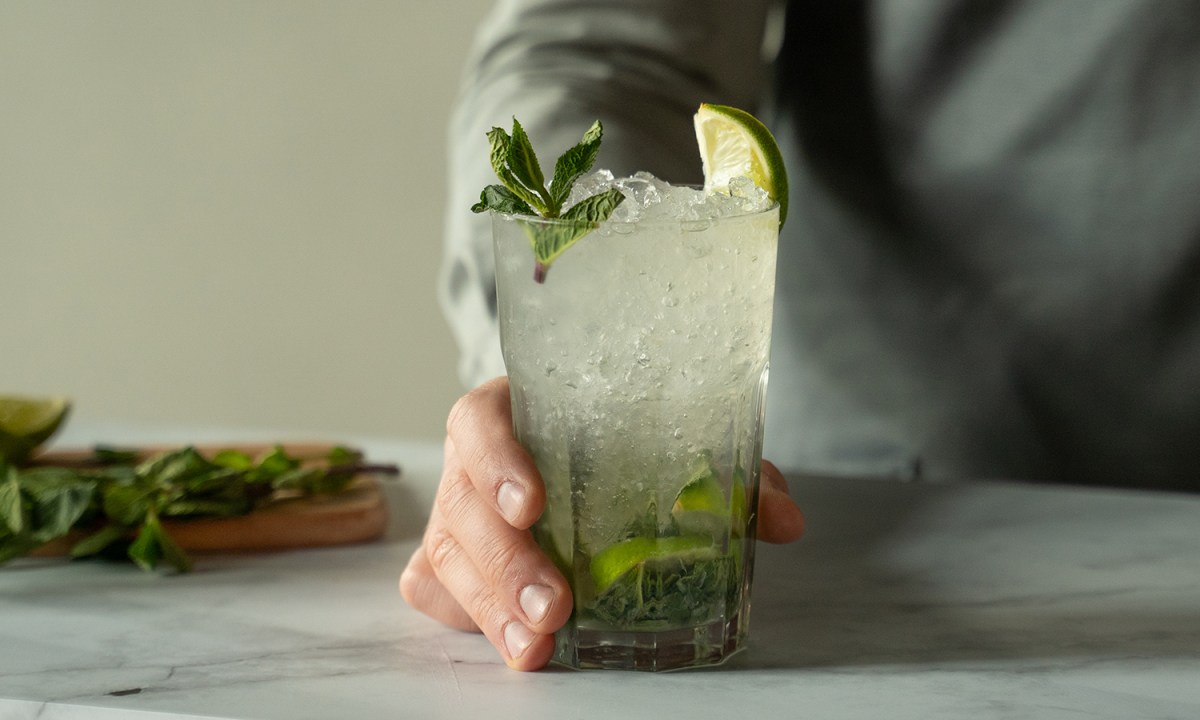 A hand serving a glass of Mojito on a table.