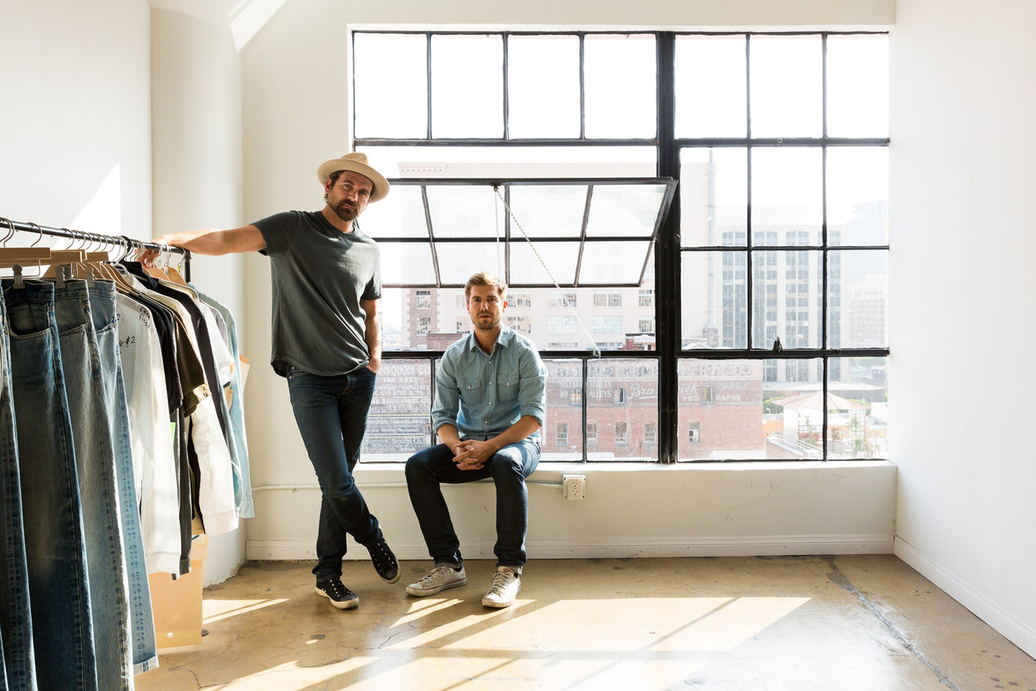 Two men standing near a clothing rack.