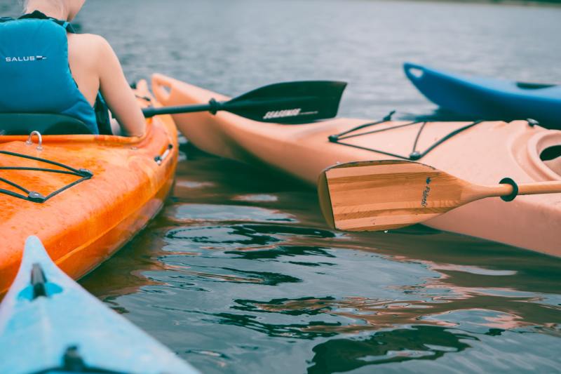 Person riding on orange kayak during daytime with other kayakers