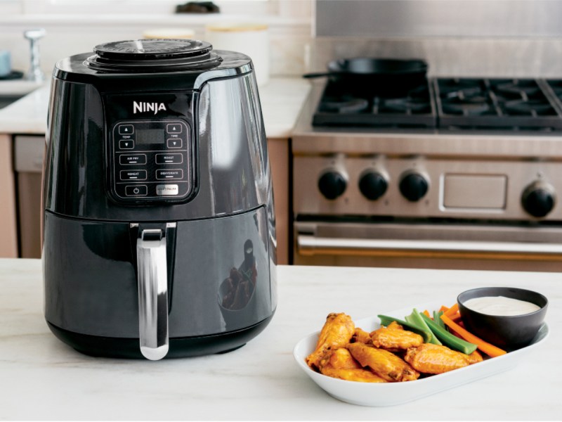 Ninja Af1oo air fryer on a kitchen counter with plate of fried chicken wings next to it.