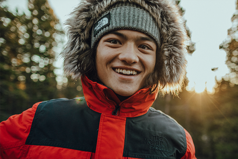 Smiling person in a North Face beanie and winter coat outdoors.