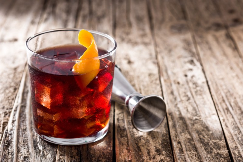 Boulevardier cocktail and orange zest on wooden table