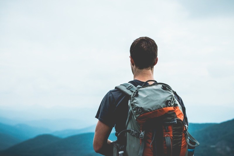 man with backpack facing mountains