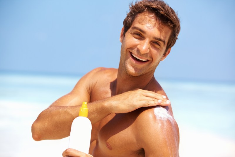 Portrait of attractive young man applying sunscreen lotion on body