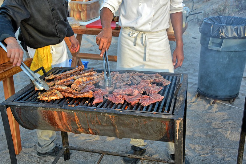Two men grilling slabs of meat on a grill outdoors.