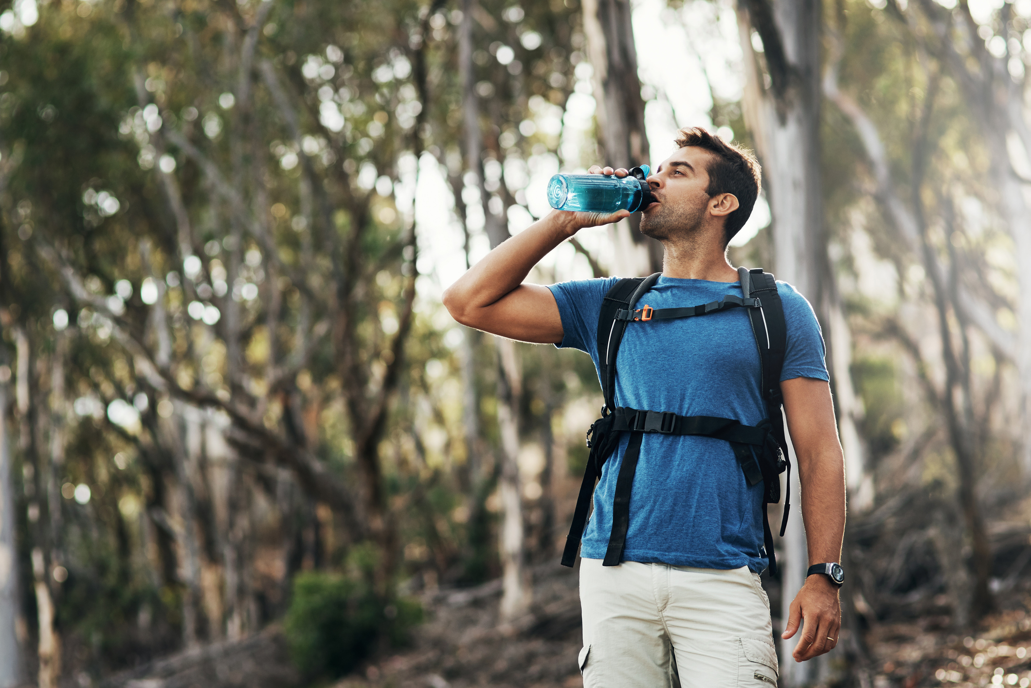 A carefree young man drinks water from a bottle while going for a hike up a mountain